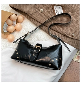 Détail d'un sac d'épaule en cuir verni noir avec rivets punk et boucle métal sur dentelle