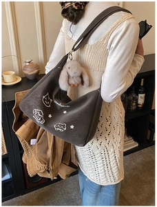 Detalle de bolso bandolera marrón oscuro con bordado de gato y colgante de conejo