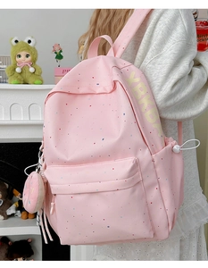 Pink student backpack with colorful speckle pattern and donut charm detail in home setting