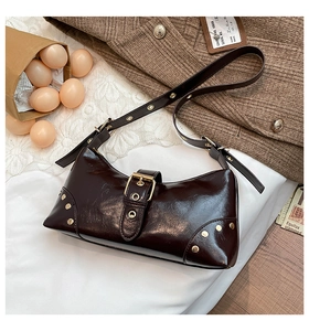 Détail d'un sac à bandoulière en cuir marron brillant avec rivets punk et boucle Y2K