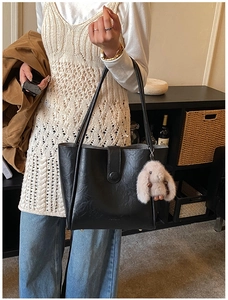 Detail of black faux leather tote bag with a plush bunny charm and secure buckle closure
