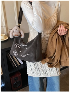 Detalle del bolso de hombro café con bordado de gato y colgante de conejo de peluche