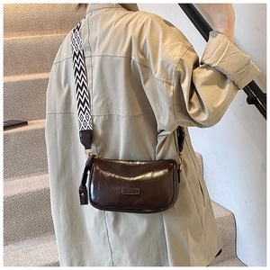 Detail of dark brown glossy shoulder bag with a patterned wide fabric strap