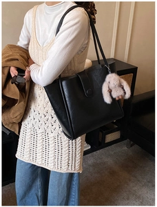 Detail of a black faux leather tote bag with vertical magnetic flap and rabbit charm