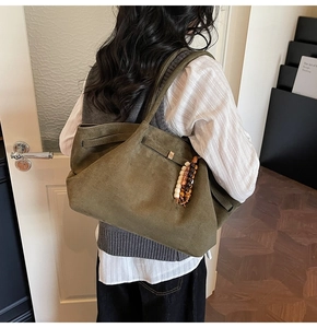 Detail of olive green suede tote bag with ethnic bead charm and side buckle detail