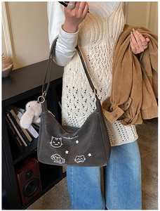 Detalle de bolso hobo de ante marrón con ilustración de gato y colgante de peluche