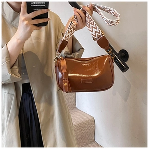 Detail of a brown glossy patent leather pillow bag with a geometric pattern strap