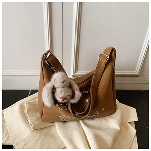 Detalle de bolso hobo marrón con bordado, hebilla dorada y amuleto de conejo de peluche