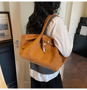 Detail of a large brown suede tote bag with belt buckle and wooden bead tassel