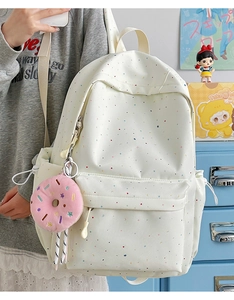 Detail of a beige canvas backpack with colorful star patterns and a pink donut charm
