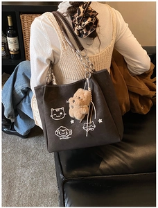 Dettaglio di una borsa tote marrone con stampa di gatto bianco e ciondolo di peluche