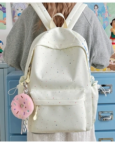 Rear view of a white student backpack with colorful dots and a plush donut charm