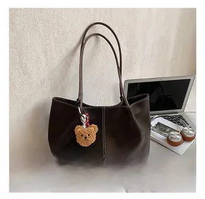 Detail of dark brown suede tote bag with plush bear charm and urban commute styling