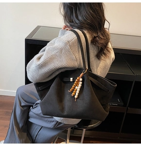 Detail of black suede tote bag featuring adjustable side drawstrings and wooden bead charm