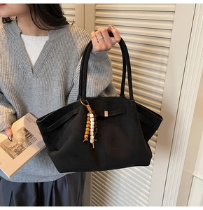 Detail of black suede tote bag with wooden beaded pendant shown on model shoulder
