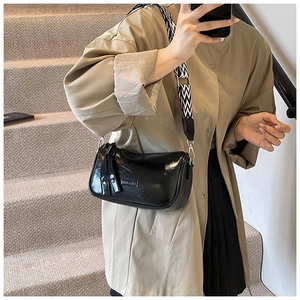 Detail of black glossy leather pillow bag with stylish black and white wave pattern strap