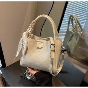 Detail of cream bucket bag with lychee texture, woven handle and decorative floral scarf
