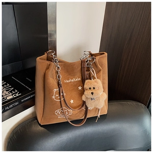 Dettaglio della borsa tote in pelle marrone con catena in metallo e ciondolo orsetto