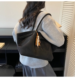 Macro detail of black matte tote bag with ethnic beaded tassel and soft texture finish