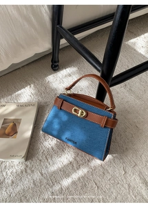 Detail of blue denim retro handbag with brown leather straps leaning on a chair