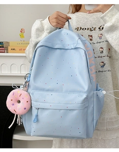 Detail of light blue polka dot student backpack featuring a cute donut charm and pockets