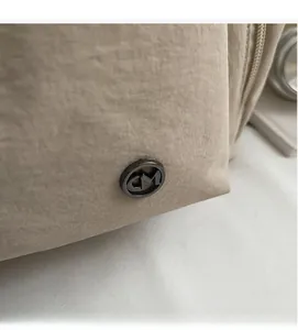 Detail einer beigen Nylon-Einkaufstasche mit rundem CM-Logo aus Metall und Textur