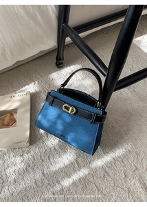 Detail of blue denim handbag featuring black leather straps and gold metal clasp