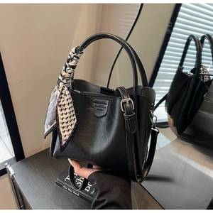 Detail of black leather bucket bag featuring a decorative silk scarf and removable strap