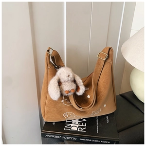 Detalle de bolso bandolera caramelo con bordado de gato y colgante de conejo de peluche