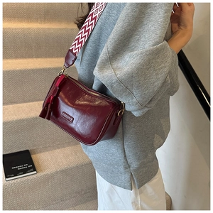 Detail of burgundy patent leather pillow bag featuring a patterned wide strap and tassel