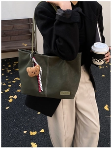 Detail of dark green leather tote bag with white stitching and brown plush bear charm
