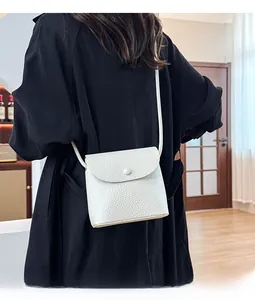 Detail of white pebbled leather crossbody bag featuring a flap closure and button