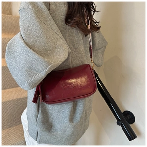 Detail shot of a glossy burgundy leather crossbody bag worn on a minimalist indoor staircase