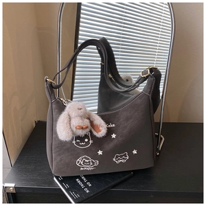 Detalle de bolso bandolera de ante gris con bordado de gato y colgante de peluche