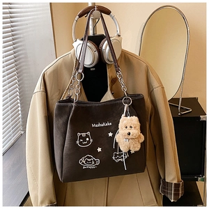 Dettaglio borsa tote in tela con gatti e tracolla a catena su un trench color kaki