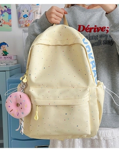 Detail of light beige polka dot backpack with a pink donut pendant and blue side strap logo