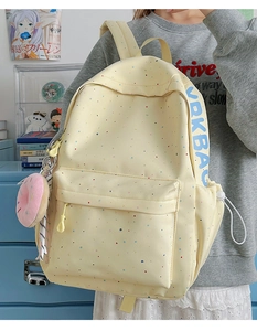 Side view of yellow waterproof backpack with colorful dots and pink donut plush pendant