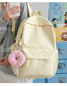 Close-up of a pale yellow backpack with star prints and a pink donut charm in a room