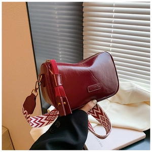 Detail of burgundy glossy leather handbag featuring HUIZENB logo and geometric strap