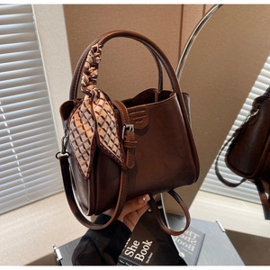 Detail of a dark brown vintage bucket bag with a decorative scarf and fashion bags logo