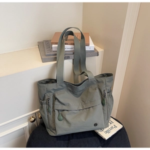 Détail d'un sac cabas en nylon vert avec poche zippée et compartiments latéraux à cordon
