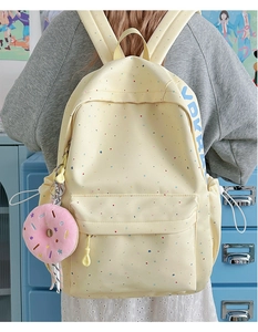 Detail of yellow canvas backpack with colorful dots, side pocket and pink donut pendant