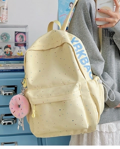 Detail view of yellow canvas backpack with colorful speckles and pink donut plush charm
