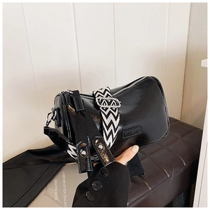 Close-up of black glossy leather pillow bag with herringbone strap and fringe detail
