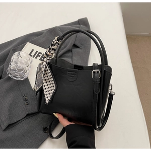 Détail du sac seau en cuir noir avec foulard en soie décoratif et fermoir métallique