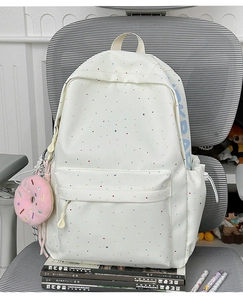 Detail of white star pattern canvas backpack with pink donut plush keychain on a chair