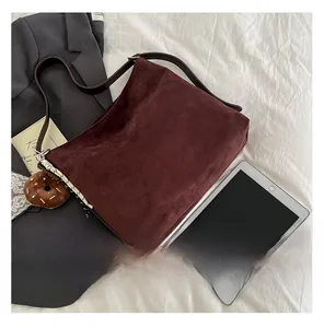 Detail of burgundy suede tote bag featuring brown leather straps and donut plush charm