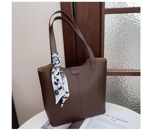 Detail of dark brown pebble leather tote bag with floral silk scarf on white table