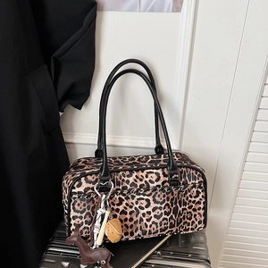 Detalle de bolso de leopardo con asas negras y colgante de caballo sobre maleta plateada