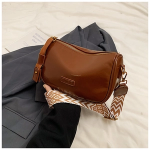 Brown leather pillow bag with a colorful geometric woven wide shoulder strap and gold zipper